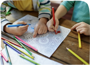 Children coloring a detailed nature-themed coloring page with colored pencils on a wooden table