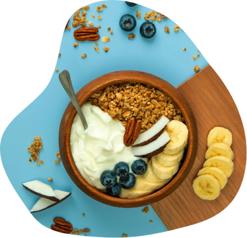 Wooden bowl with granola, yogurt, banana slices, blueberries, coconut, and pecans on blue and wooden surface
